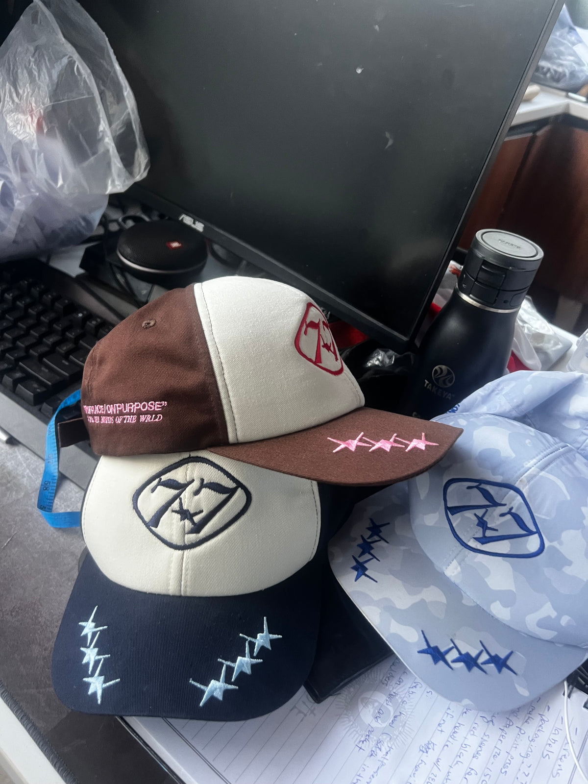 77 Emblem Caps stacked, Mocha – Rose showing the embroidered side text and Navy – Sky below